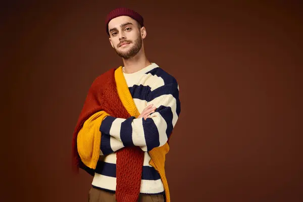 A trendy young man shows off his style in a beanie and colorful layers against a warm backdrop. — Stock Photo
