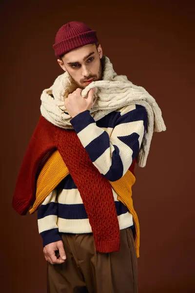 Handsome young man demonstrates his fashion sense in a studio, wearing layered knitted garments. — Stock Photo