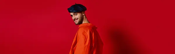 Romantischer junger Mann mit Baskenmütze posiert selbstbewusst in einem leuchtend roten Studio-Setting, Banner — Stockfoto