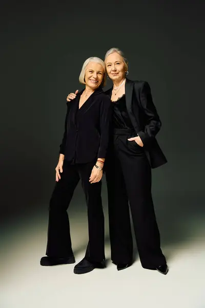 Two mature women dressed in chic black outfits radiate love and elegance in a bold studio space. — Stock Photo