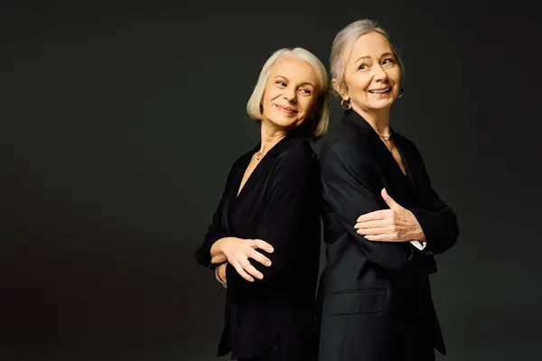 Two stylish women stand back to back, radiating elegance and love in a minimalist atmosphere. — Stock Photo