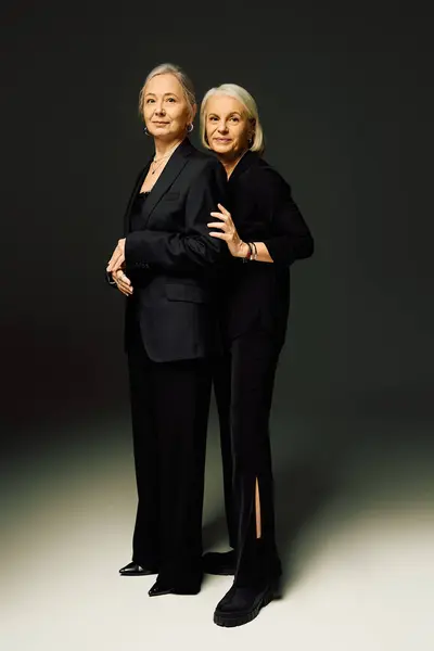 Two fashionable women share a tender moment, exuding elegance with their stylish outfits and smiles. — Stock Photo