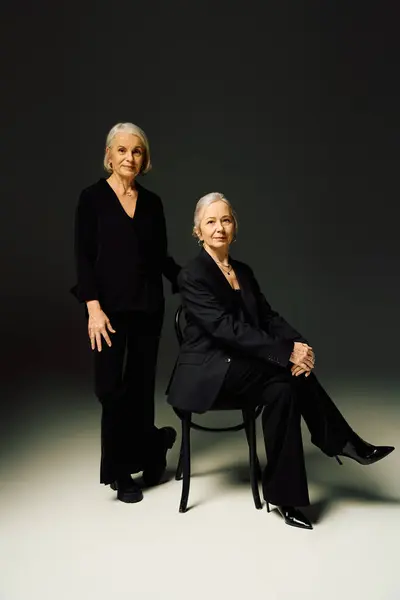 Two stylish mature women stand together in a chic studio, radiating love and confidence. — Stock Photo