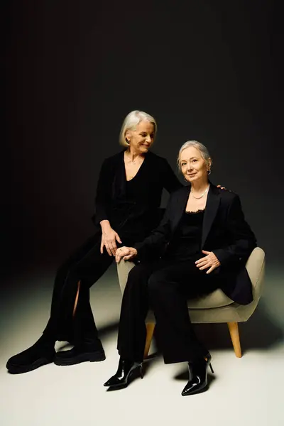 Two fashionable mature women sit together, exuding love and confidence in a stylish setting. — Stock Photo