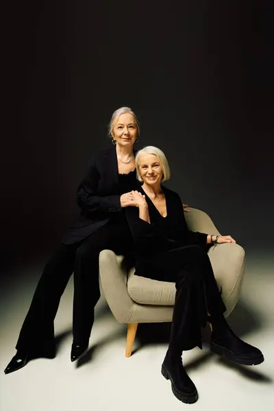 Two fashionable women share a warm embrace while sitting together on a chic chair, radiating joy. — Stock Photo