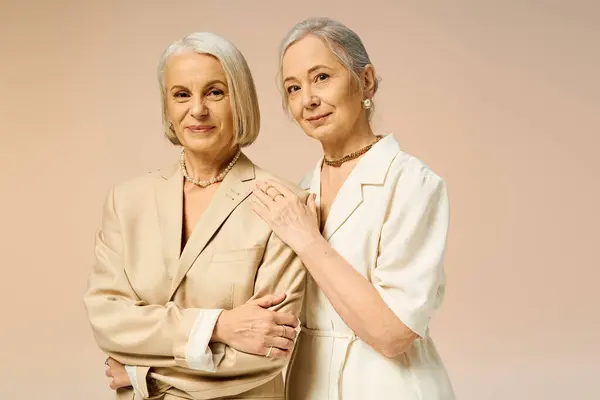 Two mature women showcase their love and fashion sense in a contemporary, soft toned backdrop. — Stock Photo