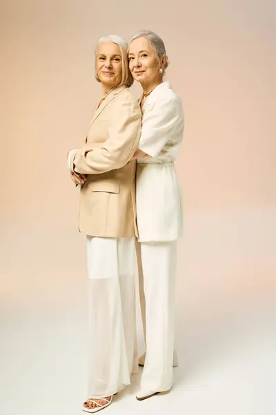 Two fashionable mature women stand elegantly back to back, embodying love and stylishness. — Foto stock