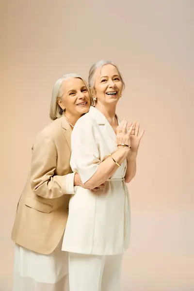 Two stylish mature women joyfully embrace, highlighting their love and fashion in a warm setting. — Stock Photo