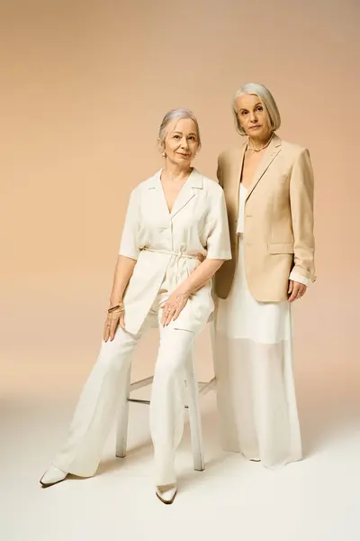 Two women exude grace and style, dressed in chic outfits against a soft pastel backdrop. — Stock Photo