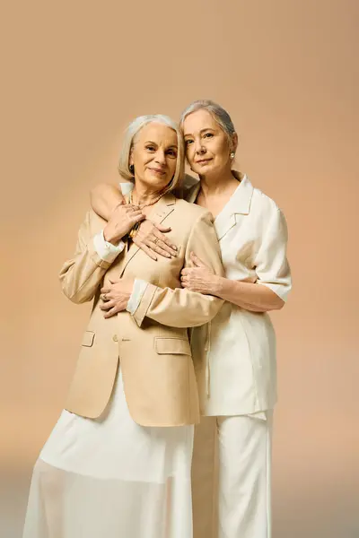 Two mature women share a loving embrace, showcasing their fashionable styles amidst a warm backdrop. — Stock Photo