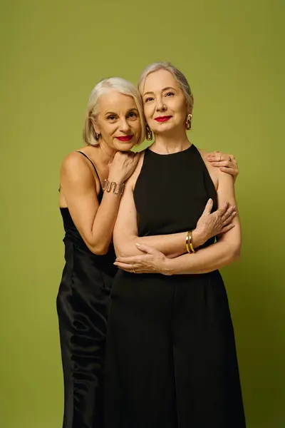 Two fashionable mature women embrace each other joyfully against a lively green backdrop. — Stock Photo