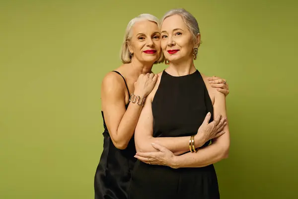 Two mature women showcase their love and style against a lively green backdrop. — Stock Photo