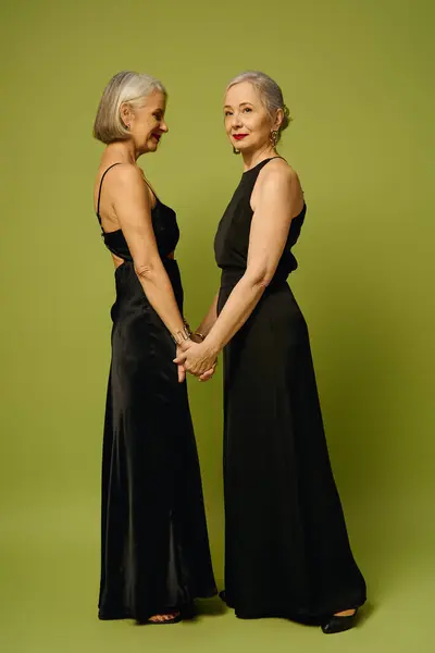 Zwei modische Frauen halten sich an den Händen, verströmen Zuversicht und Romantik vor leuchtend grünem Hintergrund. — Stockfoto