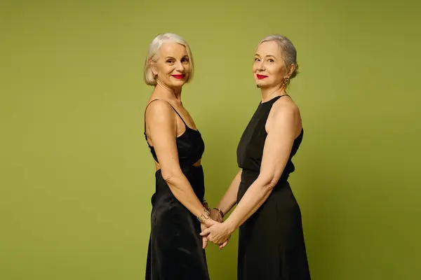 Two fashionable mature women hold hands, showcasing their elegance and romance in a lively setting. — Stock Photo