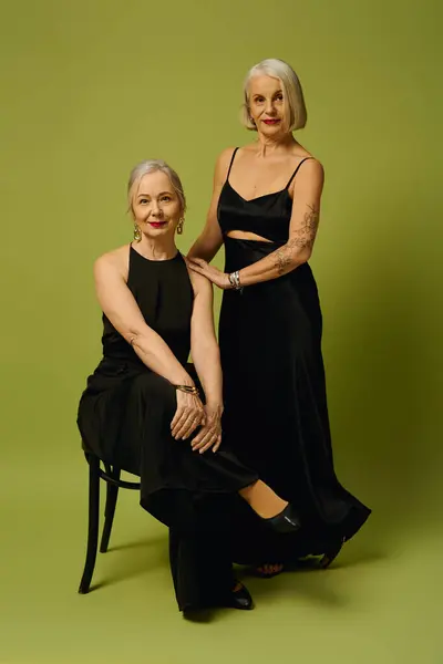 Two stylish mature women radiate romance and confidence in chic black outfits on a green backdrop. — Photo de stock