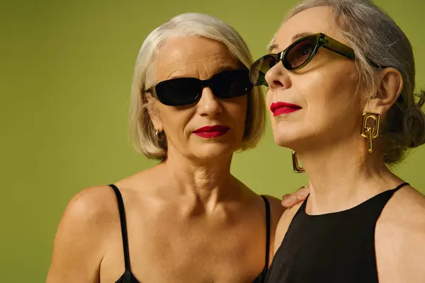 Two mature women express love and elegance, adorned in chic sunglasses against a vivid backdrop. — Stock Photo