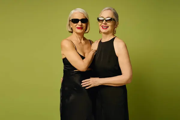 Two stylish mature women embrace joyfully, showcasing their love in fashionable black dresses. — Stock Photo