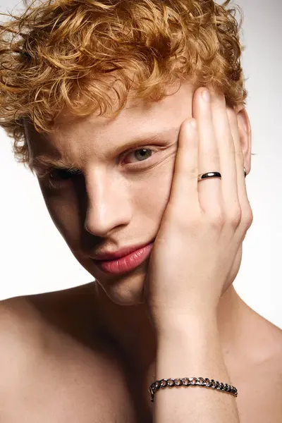 Confident young man with curly hair rests his chin on his hand while striking a fashionable pose. — Stock Photo
