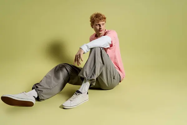 A fashionable young man with curly hair relaxes in a stylish outfit on a smooth pastel surface. — Stock Photo