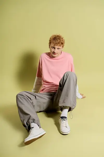 A stylish young man leans against a pastel background, exuding a relaxed, fashionable vibe. — Stock Photo