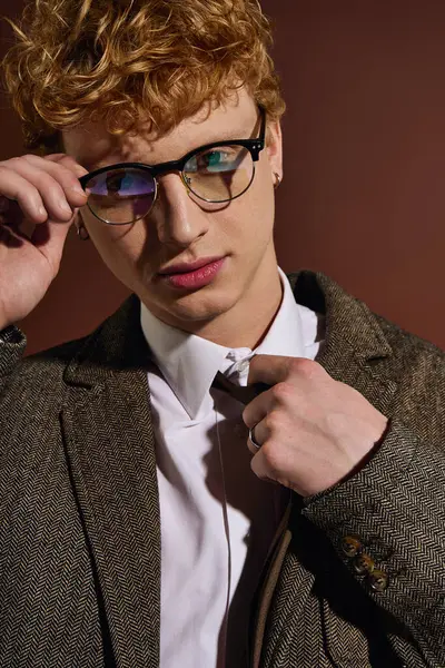 A young handsome man with curly hair and glasses is adjusting his tie in a fashionable studio. — Stock Photo