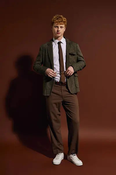 A young man dressed in trendy attire stands confidently against a warm backdrop, exuding charm. — Stock Photo