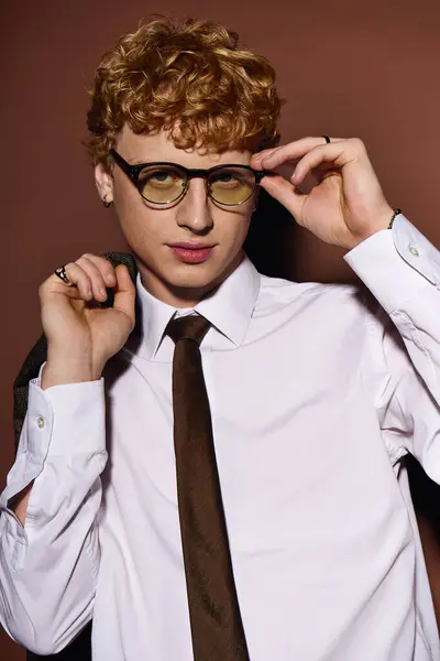 A young man adjusts his glasses, exuding confidence in his stylish outfit. — Stock Photo