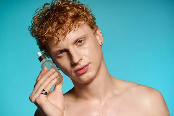 Schöner junger Mann hält eine Serumflasche in der Hand, die Stil und Charme in heller Umgebung ausstrahlt. — Stock Photo