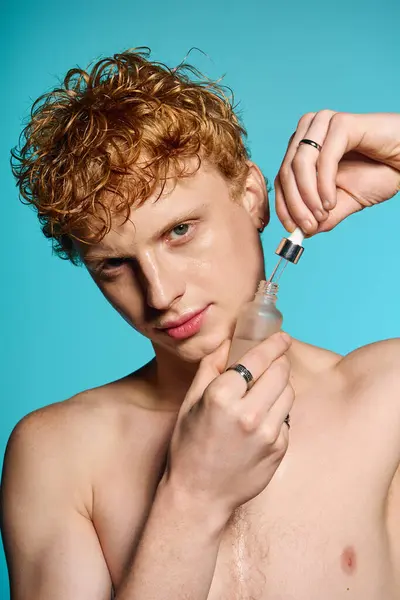 Young man with curly hair confidently applies skincare against a vibrant backdrop. — Stock Photo