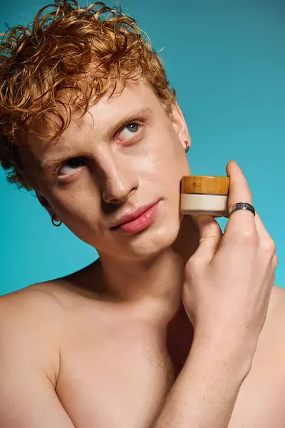 A trendy young man showcases a skincare jar and his style against a bright backdrop. — Stock Photo