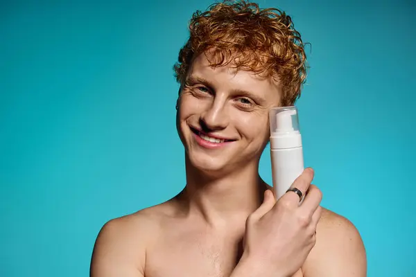 Confident young man showcases a skincare product with a bright smile and trendy hair. — Stock Photo