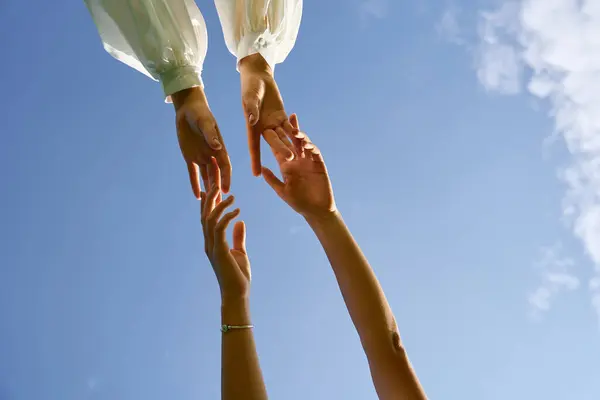Two graceful hands reach for each other against a clear blue sky, symbolizing connection. — Stock Photo