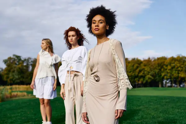 Three fashionable women embody confidence and style in a vibrant park during spring. — Stock Photo