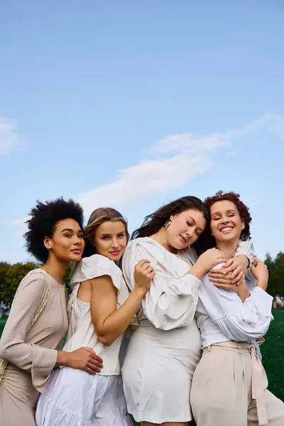 Four stylish women hug in a sunny park, celebrating confidence and friendship this spring. — Stock Photo