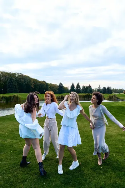 Friends dance and laugh in trendy outfits at a lush green park in spring. — Stock Photo