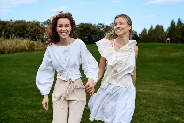 Two stylish women walk hand in hand, radiating confidence in a sunlit park during spring. — Stock Photo