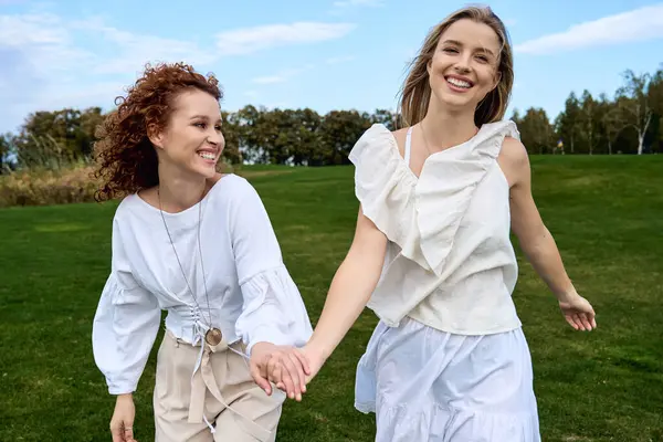 Two stylish friends stroll hand in hand through a sunny park, radiating confidence and beauty. — Stock Photo