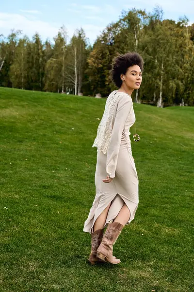 A fashionable woman walks gracefully in a chic outfit on a lush green lawn under a clear sky. — Stock Photo