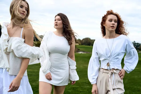 Three stylish women confidently stroll through a vibrant park in their spring outfits. — Stock Photo