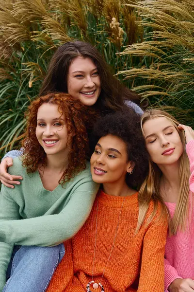 Four fashionable women smile together in a sunlit park surrounded by lush greenery. — Stock Photo