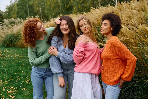 Quatre femmes élégantes embrassent l'amitié tout en mettant en valeur leur sens de la mode dans un parc extérieur luxuriant. — Photo de stock