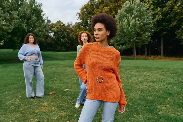 Three stylish women showcase their trendy spring outfits in a lush outdoor park, exuding confidence. — Stock Photo