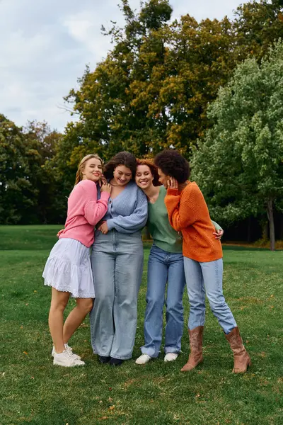 Four fashionable women share joyful moments in a lush green park, celebrating friendship outdoors. — Stock Photo