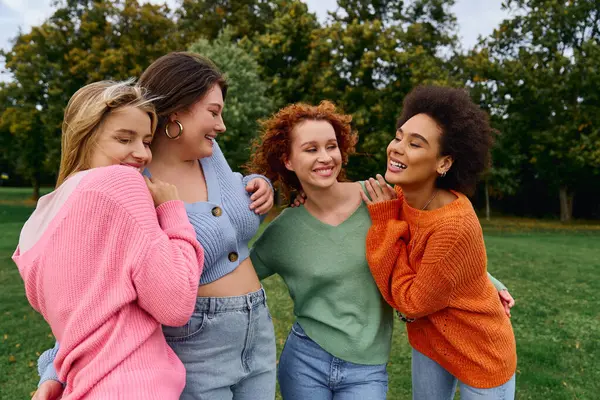 Un groupe animé de quatre femmes élégantes embrasse la chaleur du printemps dans un cadre de parc extérieur. — Photo de stock