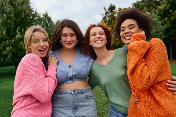 Quatre femmes à la mode embrassent la fraîcheur du printemps dans un beau parc, rayonnant de confiance. — Photo de stock