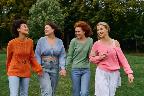 Four fashionable friends walk confidently through a sunny park, enjoying natures beauty. — Stock Photo