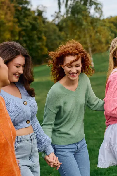Friends in stylish outfits stroll hand in hand through a lush park, radiating confidence and joy. — Stock Photo