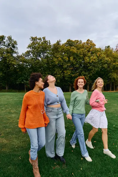 Quatre femmes à la mode marchent en toute confiance dans un parc animé, célébrant l'amitié sous un ciel bleu. — Photo de stock