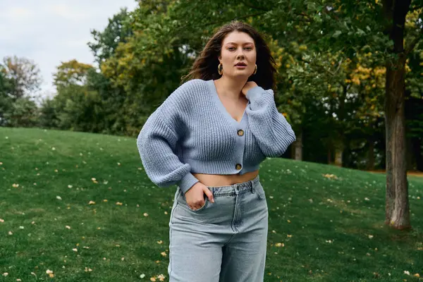 Una donna elegante si trova con fiducia in un parco verde, in mostra il suo vestito alla moda. — Foto stock