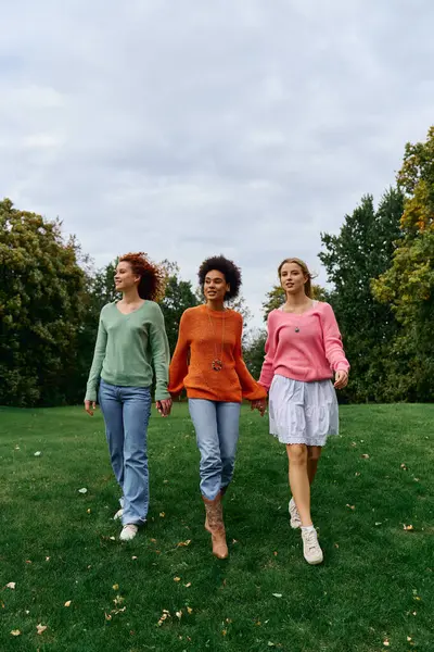 Three stylish women walk hand in hand through a lush green park, exuding confidence and charm. — Stock Photo